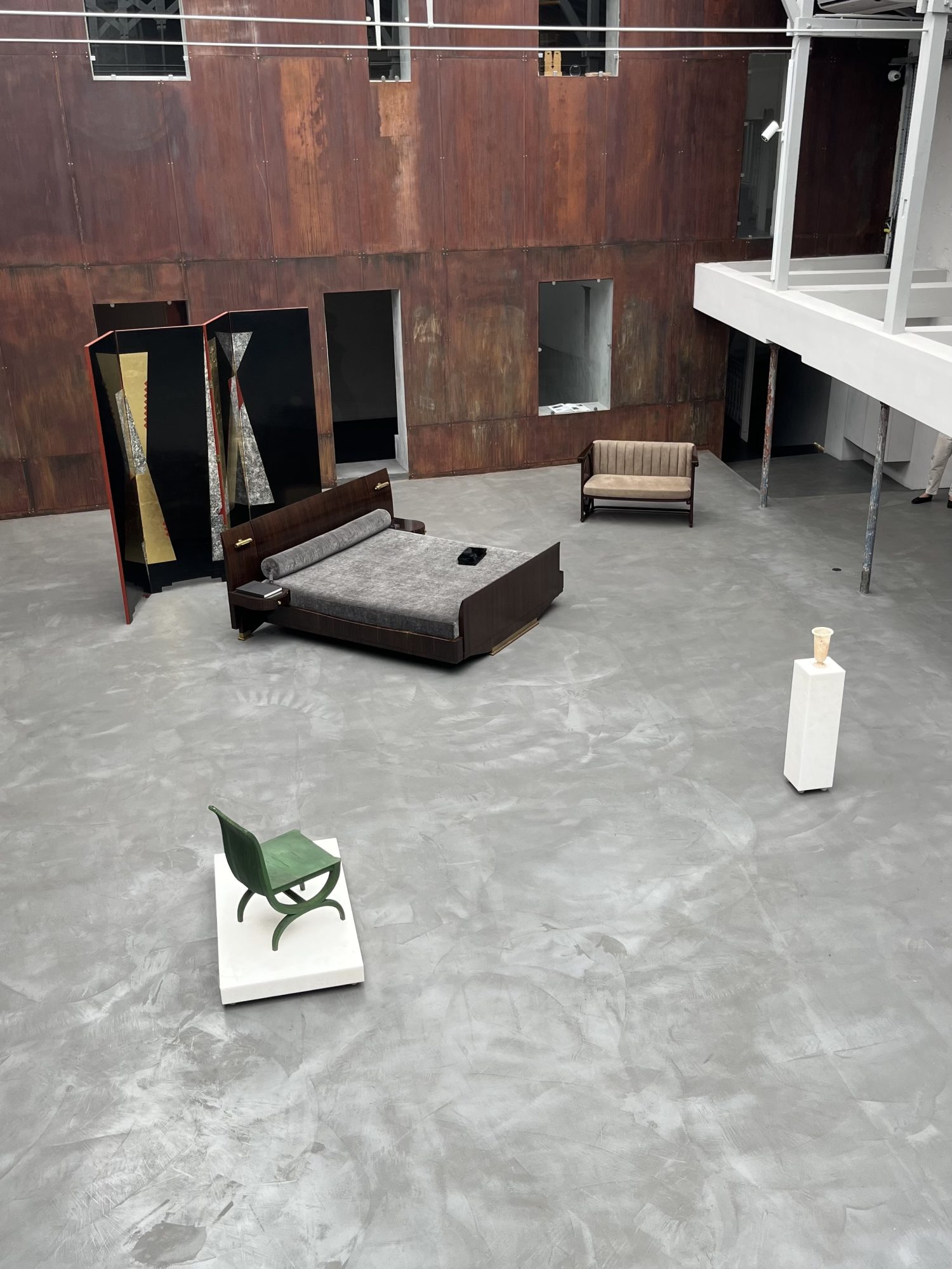 Installation view of Forms and Temptations at Sceners Gallery, Paris, showing a large grey-floored gallery with early twentieth-century furniture and decorative objects arranged across the space, including a bed, screen, sofa, small pedestal object and green chair.